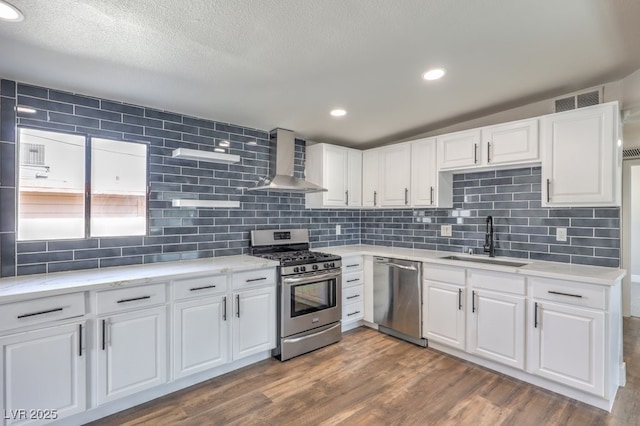 kitchen featuring wall chimney exhaust hood, stainless steel appliances, tasteful backsplash, white cabinetry, and sink