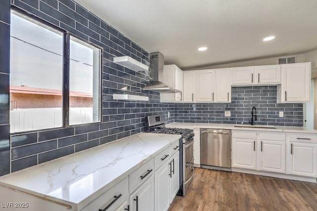 kitchen featuring sink, wall chimney range hood, white cabinetry, and appliances with stainless steel finishes