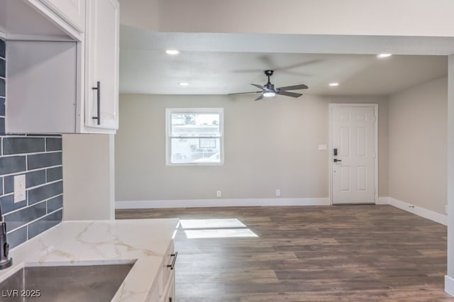 kitchen with light stone countertops, dark hardwood / wood-style floors, decorative backsplash, white cabinets, and ceiling fan