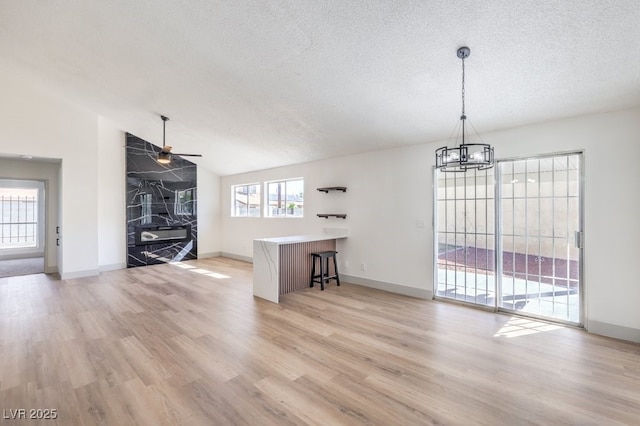 unfurnished living room featuring lofted ceiling, ceiling fan with notable chandelier, a textured ceiling, and light hardwood / wood-style flooring