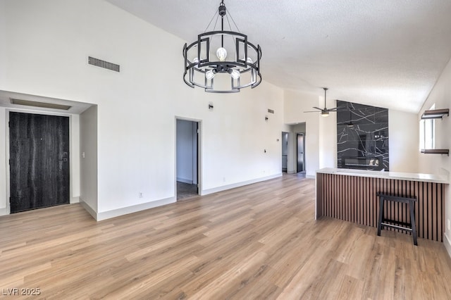 kitchen with a textured ceiling, light hardwood / wood-style flooring, decorative light fixtures, high vaulted ceiling, and ceiling fan with notable chandelier