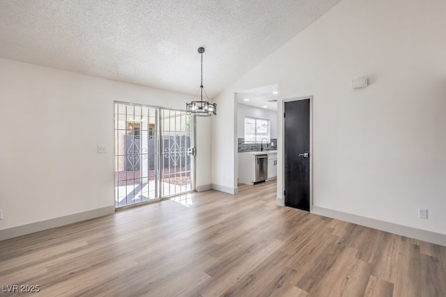 unfurnished dining area with a textured ceiling, a chandelier, lofted ceiling, light wood-type flooring, and sink