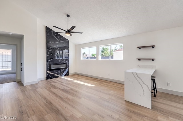 unfurnished living room with lofted ceiling, light wood-type flooring, a textured ceiling, and ceiling fan