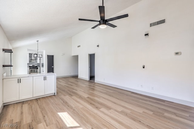 unfurnished living room featuring a textured ceiling, vaulted ceiling, light hardwood / wood-style flooring, ceiling fan with notable chandelier, and a fireplace