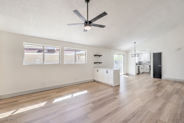 unfurnished living room featuring ceiling fan with notable chandelier, light hardwood / wood-style floors, a textured ceiling, and vaulted ceiling