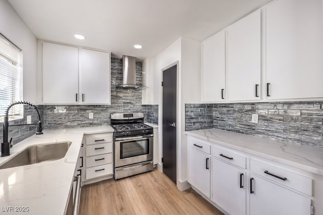 kitchen featuring sink, stainless steel range with gas stovetop, white cabinetry, and wall chimney exhaust hood