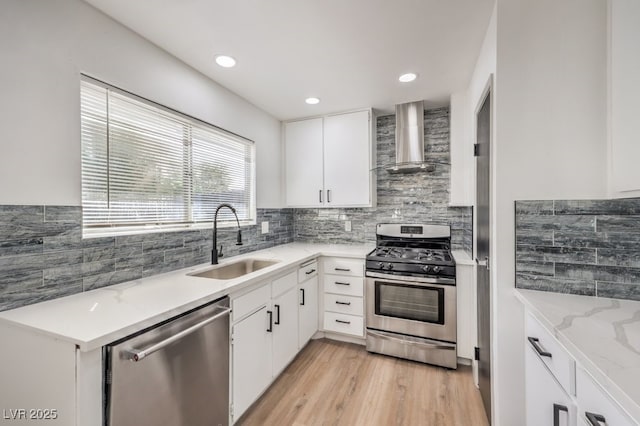 kitchen featuring stainless steel appliances, wall chimney range hood, white cabinets, and sink