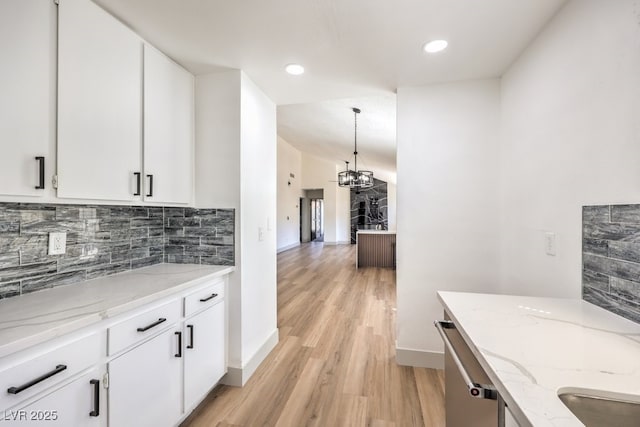 kitchen with white cabinetry, an inviting chandelier, light stone counters, light hardwood / wood-style flooring, and hanging light fixtures