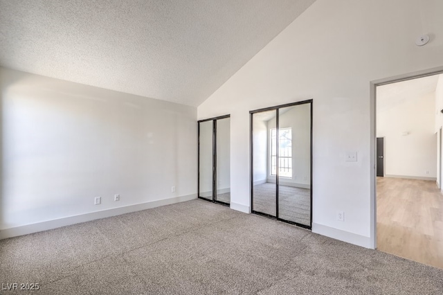 unfurnished bedroom featuring high vaulted ceiling, two closets, a textured ceiling, and light colored carpet