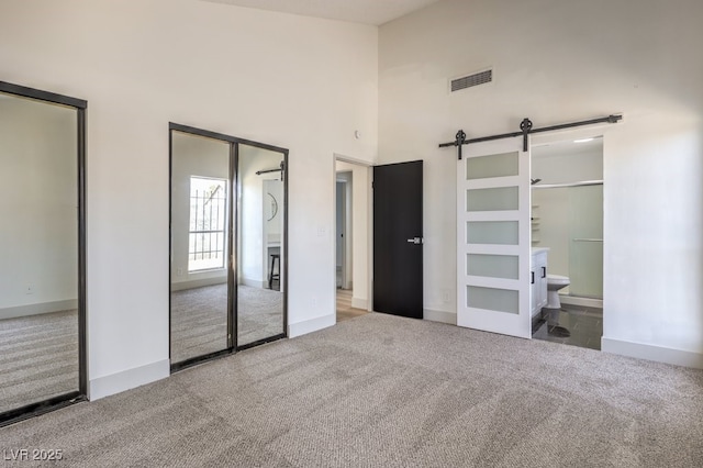 unfurnished bedroom featuring a high ceiling, ensuite bathroom, a barn door, and carpet flooring