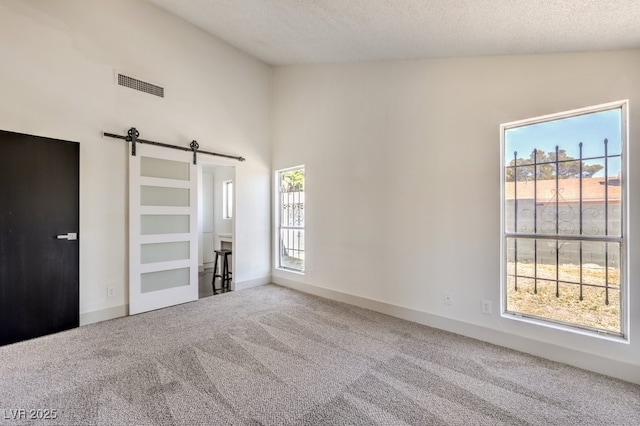 unfurnished bedroom with a textured ceiling, vaulted ceiling, a barn door, and carpet floors