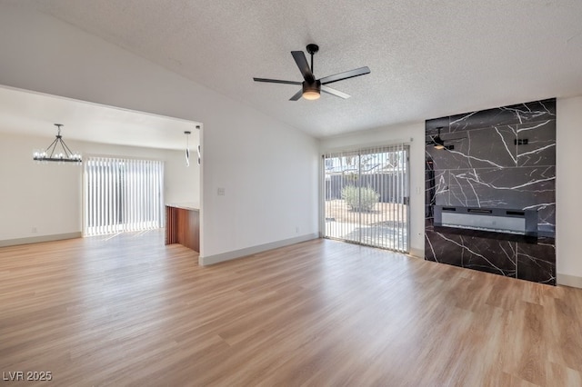 empty room with a textured ceiling, lofted ceiling, ceiling fan with notable chandelier, and hardwood / wood-style flooring