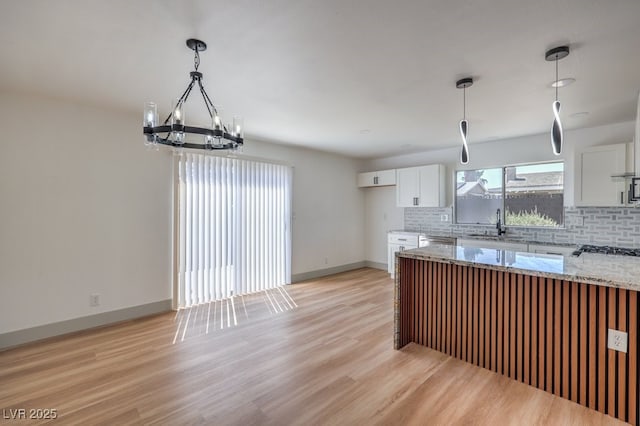 kitchen with light stone countertops, light hardwood / wood-style flooring, decorative backsplash, white cabinetry, and sink