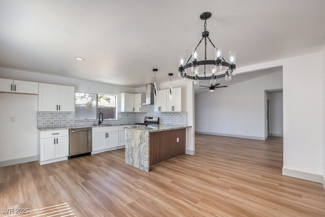 kitchen featuring stainless steel appliances, white cabinetry, light stone counters, hanging light fixtures, and wall chimney range hood