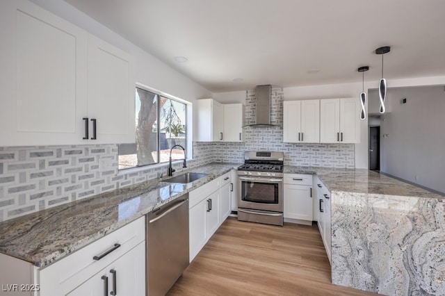 kitchen with stainless steel appliances, pendant lighting, white cabinets, wall chimney range hood, and sink