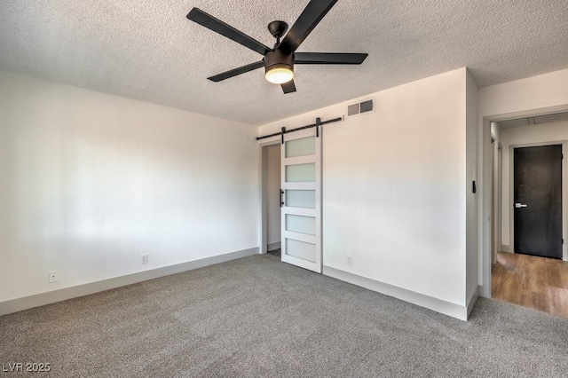 unfurnished bedroom featuring ceiling fan, a barn door, a textured ceiling, and carpet