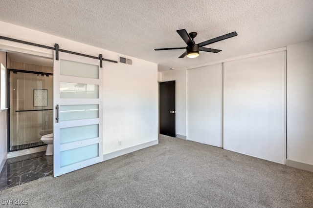 unfurnished bedroom featuring a textured ceiling, connected bathroom, ceiling fan, a closet, and a barn door