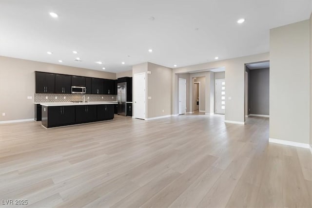 kitchen featuring an island with sink, appliances with stainless steel finishes, light wood-type flooring, and decorative backsplash