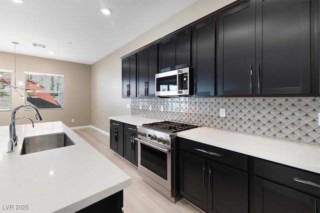 kitchen featuring sink, backsplash, stainless steel appliances, decorative light fixtures, and light wood-type flooring