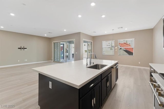 kitchen with pendant lighting, sink, appliances with stainless steel finishes, a kitchen island with sink, and light wood-type flooring