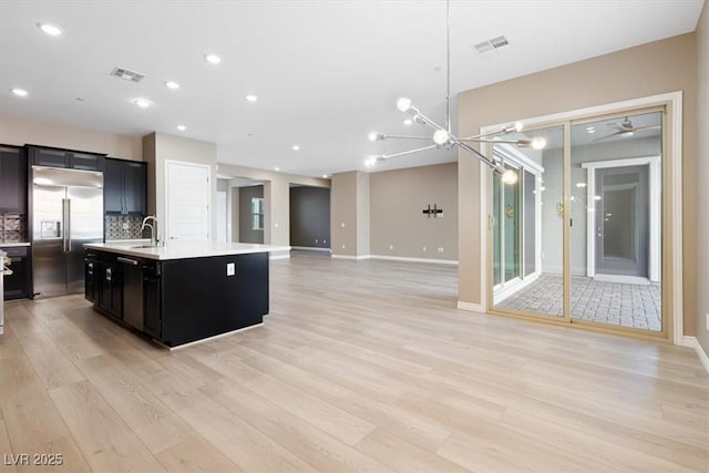 kitchen with sink, tasteful backsplash, light hardwood / wood-style floors, a center island with sink, and built in fridge