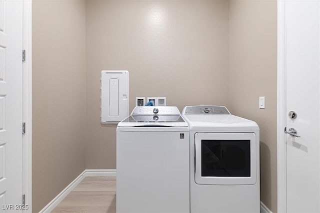 laundry room with light hardwood / wood-style flooring, washing machine and dryer, and electric panel