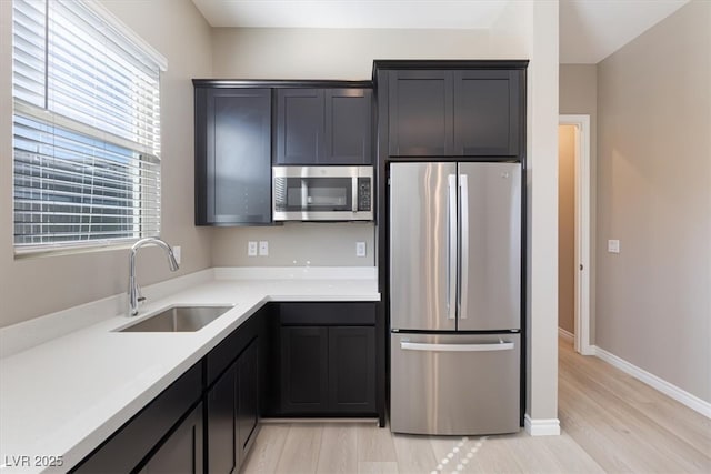 kitchen with appliances with stainless steel finishes, sink, and light wood-type flooring