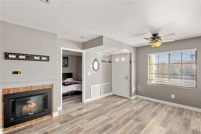 unfurnished living room featuring ceiling fan, light wood-type flooring, and a tile fireplace