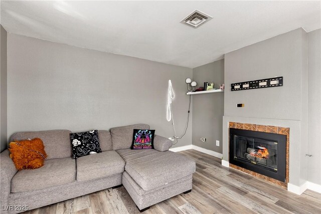 living room with a tiled fireplace and wood-type flooring