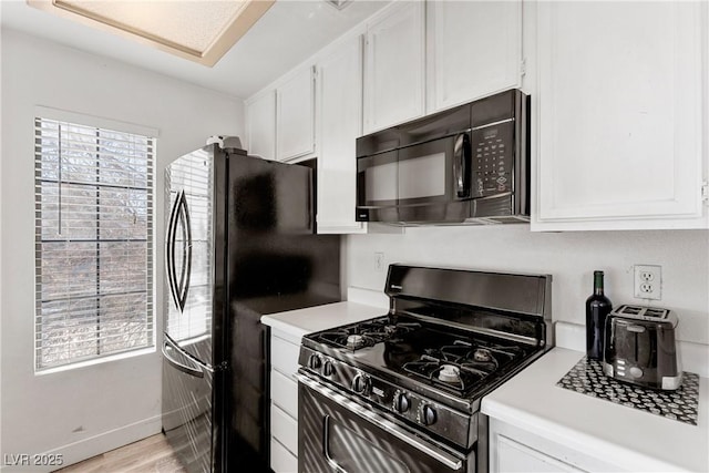 kitchen with white cabinets, light wood-type flooring, black appliances, and a healthy amount of sunlight