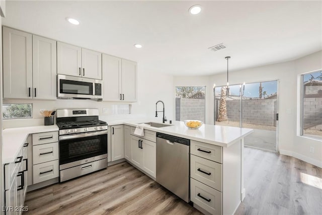 kitchen featuring appliances with stainless steel finishes, light hardwood / wood-style floors, kitchen peninsula, pendant lighting, and sink