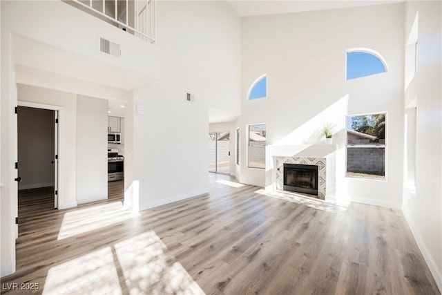 unfurnished living room featuring a towering ceiling, a tile fireplace, and light hardwood / wood-style floors