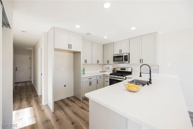 kitchen featuring kitchen peninsula, light wood-type flooring, white cabinets, appliances with stainless steel finishes, and sink