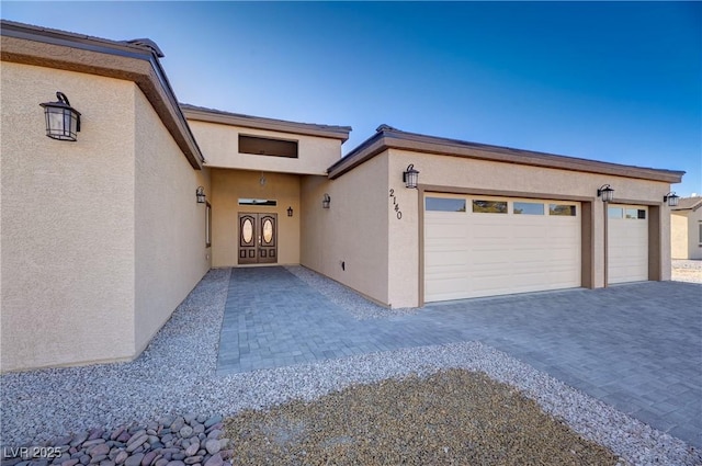 doorway to property featuring decorative driveway, an attached garage, and stucco siding