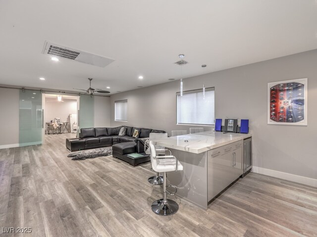 interior space with ceiling fan, light hardwood / wood-style flooring, kitchen peninsula, and hanging light fixtures