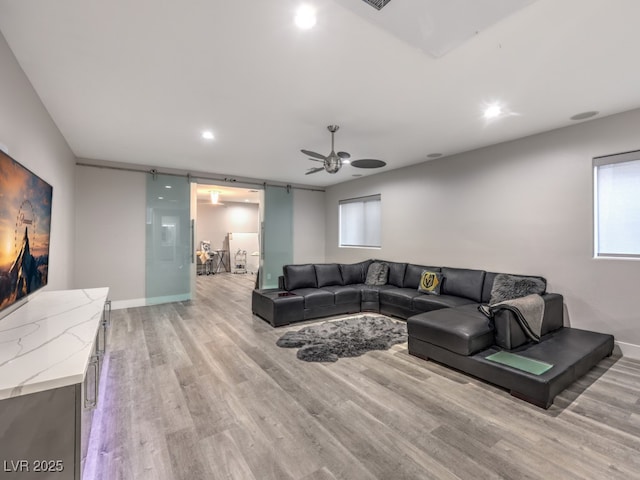 living room featuring ceiling fan, a barn door, and light wood-type flooring