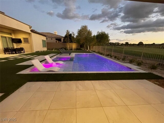 pool at dusk with pool water feature and a patio