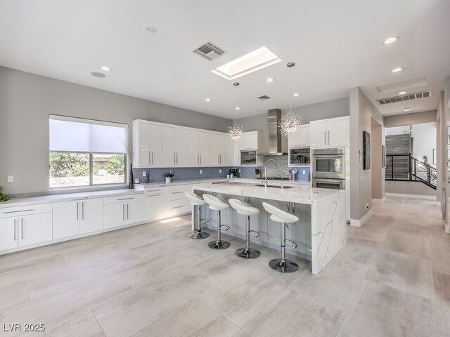 kitchen featuring white cabinetry, pendant lighting, a large island with sink, a breakfast bar, and sink