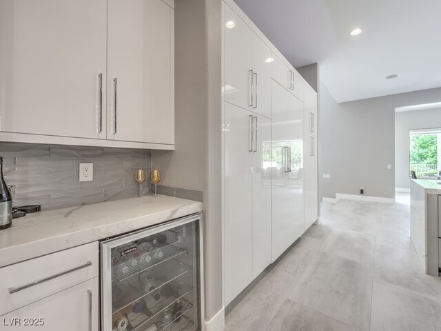 bar featuring wine cooler, white cabinets, tasteful backsplash, and light stone countertops