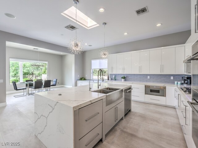 kitchen with hanging light fixtures, white cabinets, a skylight, and an island with sink