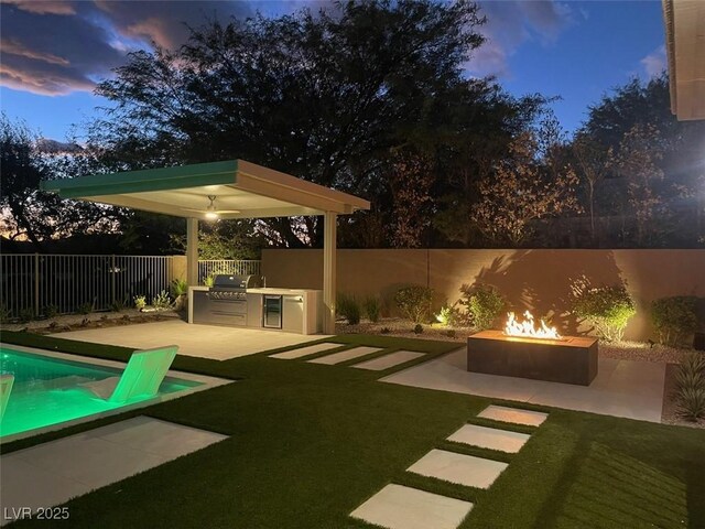 yard at dusk featuring a fenced in pool, a fire pit, exterior kitchen, and a patio