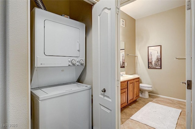 clothes washing area with sink, light tile patterned floors, and stacked washer / dryer