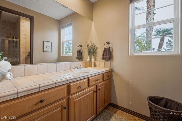 bathroom with a shower with shower door, a healthy amount of sunlight, and vanity