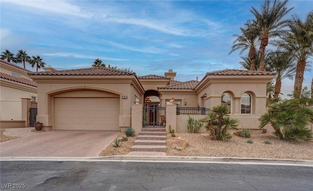 mediterranean / spanish-style house featuring a gate, fence, an attached garage, stucco siding, and decorative driveway