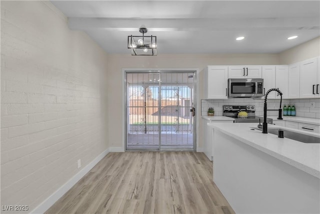 kitchen with stainless steel appliances, hanging light fixtures, sink, light hardwood / wood-style flooring, and white cabinetry