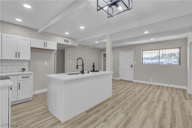 kitchen featuring sink, white cabinets, tasteful backsplash, an island with sink, and beam ceiling