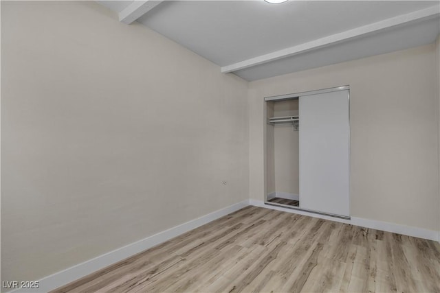 unfurnished bedroom featuring a closet, light hardwood / wood-style floors, and beamed ceiling