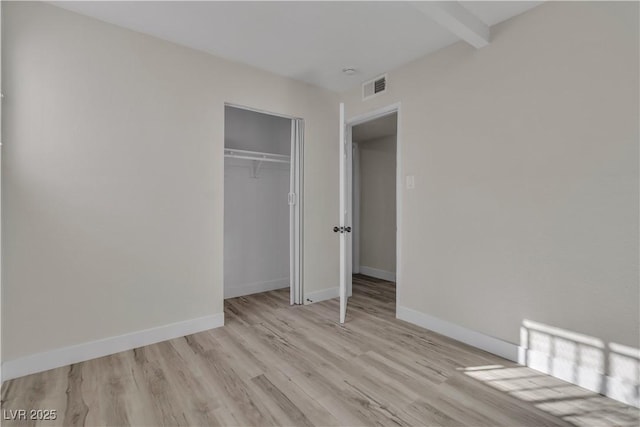 unfurnished bedroom featuring a closet, beam ceiling, and light hardwood / wood-style flooring