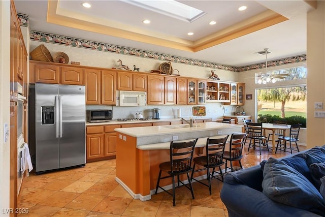 kitchen with an island with sink, a breakfast bar area, hanging light fixtures, a tray ceiling, and appliances with stainless steel finishes