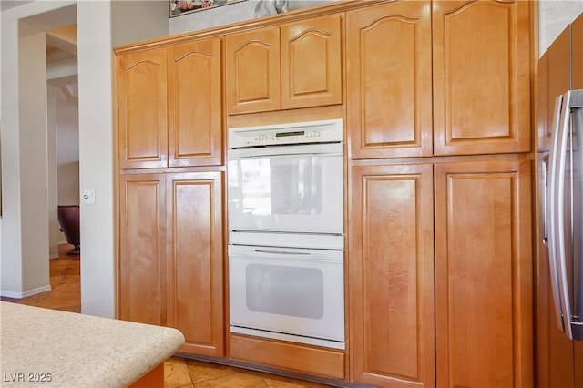 kitchen featuring stainless steel fridge, light tile patterned flooring, and white double oven